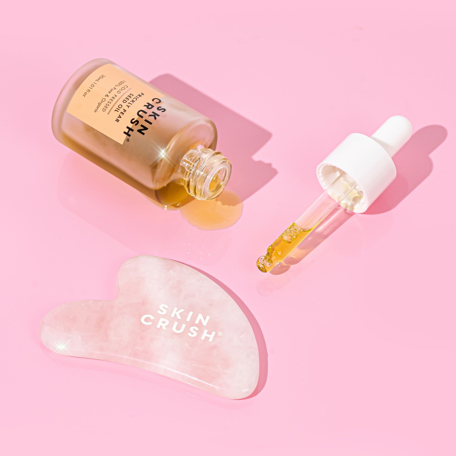 100% pure organic prickly pear seed oil and gua sha on pink background